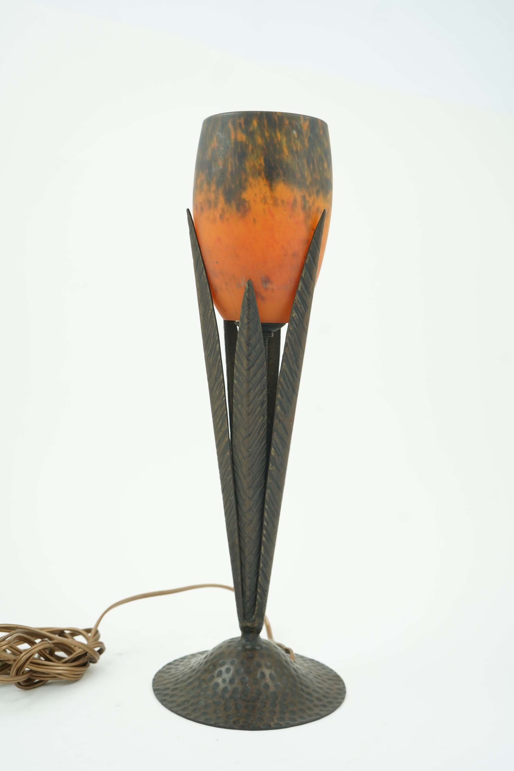 Manner of Muller Freres and Robj: A French Art Deco table lamp the mottled orange glass shade supported by naturalistic palm-leaf metal supports terminating in a circular hammered metal base, 40cm high